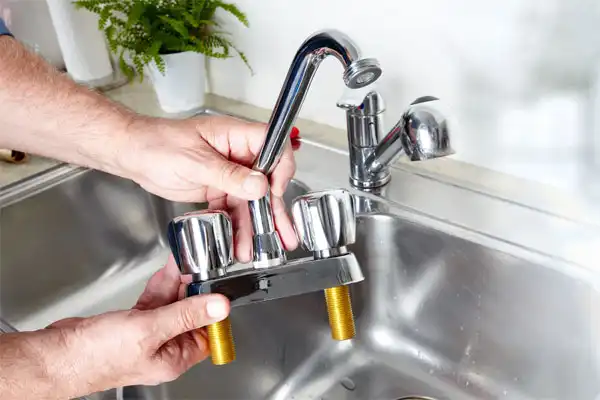 Person holding a detached kitchen faucet with two handles over a stainless steel sink.