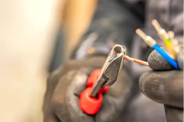 A person wearing gloves uses red-handled wire cutters to cut electrical wires.