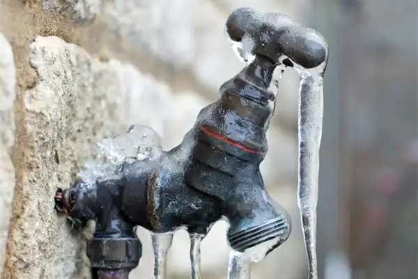 Outdoor water faucet covered in ice with several icicles hanging from it, attached to a stone wall.