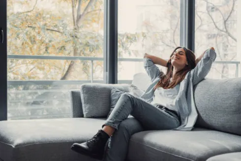 %Focuskw% | Strongbuilt Plumbing, Air, Electrical A woman relaxes on her couch by the windows, enjoying the cool air from her A/C.