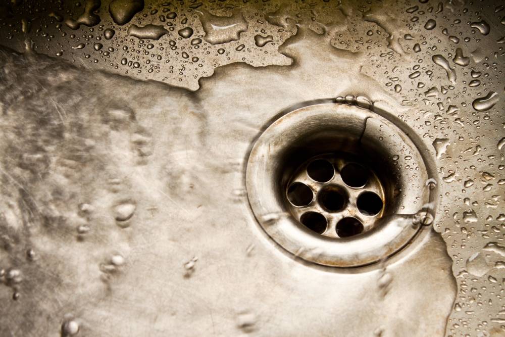 Close-up of a stainless steel sink drain with water and droplets on the surface