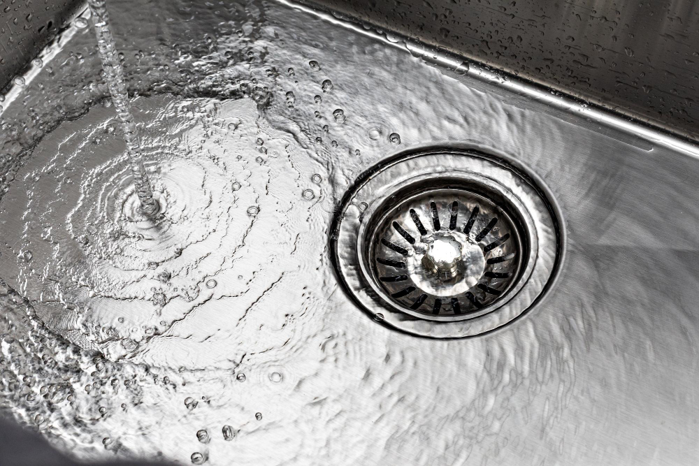 A stream of water flows into a stainless steel sink, creating ripples around the drain.