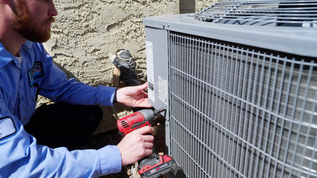 %Focuskw% | Strongbuilt Plumbing, Air, Electrical A technician uses a power drill to work on an outdoor air conditioning unit next to a textured wall.