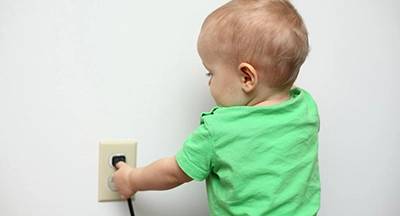 %Focuskw% | Strongbuilt Plumbing, Air, Electrical A young child wearing a green shirt is reaching toward an electrical outlet with their hand near a plug.