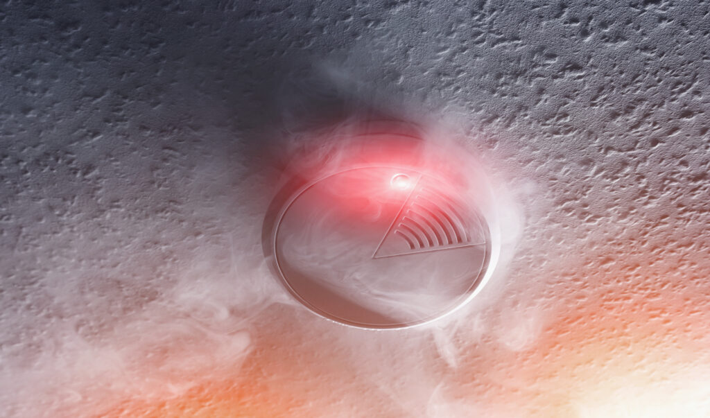 Smoke detector flashing red amid smoke, highlighting the importance of protecting your home and family from fire and carbon monoxide hazards.